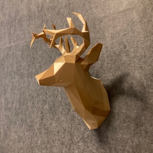 Puede incluir: Una escultura de cabeza de ciervo geométrica hecha de plástico marrón. La escultura tiene un diseño simple y moderno y es perfecta para agregar un toque de naturaleza a cualquier habitación.