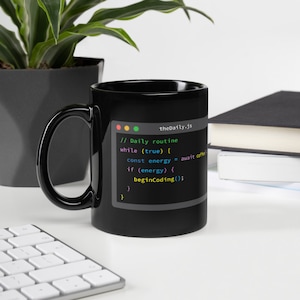 May include: Black coffee mug featuring a white design of a computer screen displaying code. The code reads "// Daily routine" and "while (true) { const energy = await coffee if (energy) { beginCoding(); } }" The code is in different colours, including pink, blue, green, and yellow.