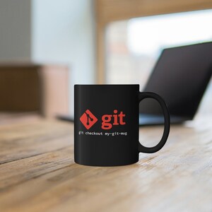 Op de afbeelding: Zwarte keramische mok met een rood Git-logo en de tekst "git checkout my-git-mug".