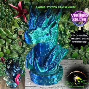 May include: A blue and green dragon head gaming station with the text "GAMING STATION DRACHENKOPF" and "VERIFIED SELLER". The dragon head is designed to hold a controller, headset, and glasses. The base has the text "Für Controller, Headset, Brille und Basecap".