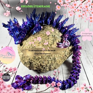 May include: A 3D printed purple and blue dragon figurine with a cherry blossom design. The dragon is curled up on a rock with pink cherry blossoms in the background. The text "Kirschblütendrache", "Exklusiver 3D Druck", "Top Designer", "Einzigartiges Blütendesing", "Authorized Seller" is visible in the image.