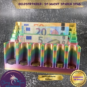 Könnte beinhalten: Ein regenbogenfarbener 3D-gedruckter Geldorganisator mit Fächern für Scheine und Münzen. Der Organizer hat ein Fach für Scheine und mehrere Fächer für Münzen. Der Text "GELDSORTIERER- SO MACHT SPAREN SPAS" ist auf der Oberseite des Organizers gedruckt. Der Text "Verschiedene Farben" ist unter dem Organizer gedruckt. Der Text "Exklusiver 3D Druck" ist auf einem goldenen Sternensticker gedruckt.