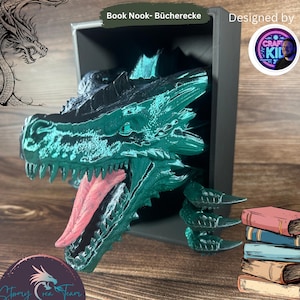 May include: A teal green dragon head bookend with a red tongue sticking out. The dragon head is partially inside a black frame. The dragon head is holding a stack of books.