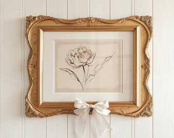 Op de afbeelding: Een ingelijste zwart-witte lijntekening van een enkele bloem met een witte satijnen strik onder het frame.