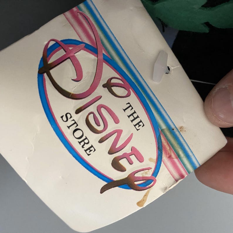May include: A white tag with a pink and gold Disney logo that says "The Disney Store" in a blue circle. The tag has a multi-colored striped border.