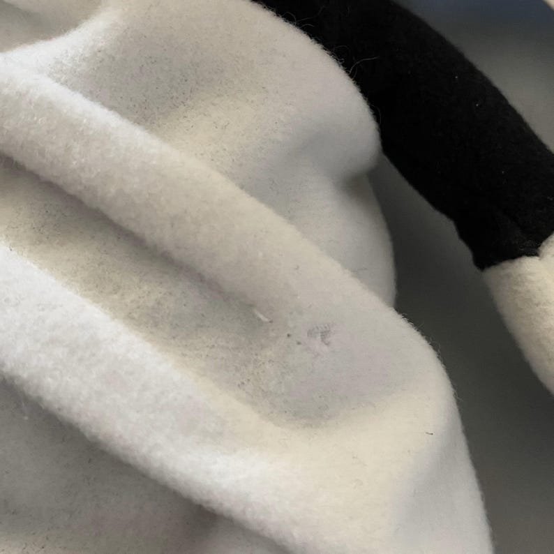 May include: Close-up of a white plush fabric with a soft, fuzzy texture. The fabric is folded and wrinkled, creating a textured surface.