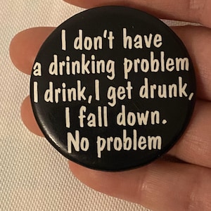 May include: A black button with white text that reads "I don't have a drinking problem I drink, I get drunk, I fall down. No problem."