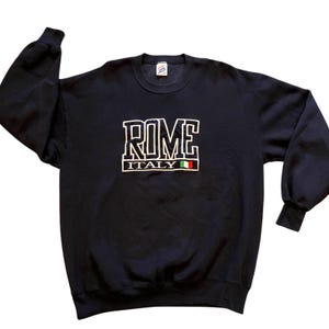 May include: Navy blue sweatshirt with the word "ROME" in white block letters, outlined in black. Below the word "ROME" is the word "ITALY" with the Italian flag. The sweatshirt has long sleeves and a crew neck.