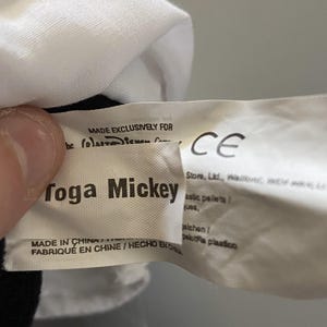 May include: White tag with black text that reads "Made Exclusively for (c) Disney Consumer Products" and "roga Mickey". Below the text is "Made in China / Fabriqu&eacute; en Chine / Hecho en China". A white tag with black text that reads "CE" is partially visible.