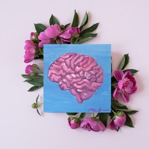 May include: A square canvas painting of a pink brain on a light blue background. The painting is surrounded by pink peonies and green leaves, set against a soft pink backdrop. The artwork is a study of the human brain.