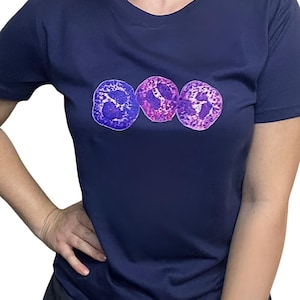 May include: Navy blue t-shirt featuring a graphic of three purple and pink cell structures. The shirt has a crew neck and short sleeves. The text "@WHITECOATARTISTRY" is at the bottom of the image.