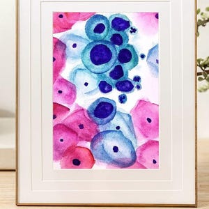 May include: Abstract watercolour painting in a white frame with a gold trim. The artwork features shapes in pink, blue, and purple. The painting is displayed on a wooden surface.