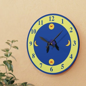 Puede incluir: Un reloj redondo azul y amarillo con una aguja negra y un dise&ntilde;o de pato de dibujos animados. Los n&uacute;meros del 1 al 12 se muestran en la esfera del reloj.