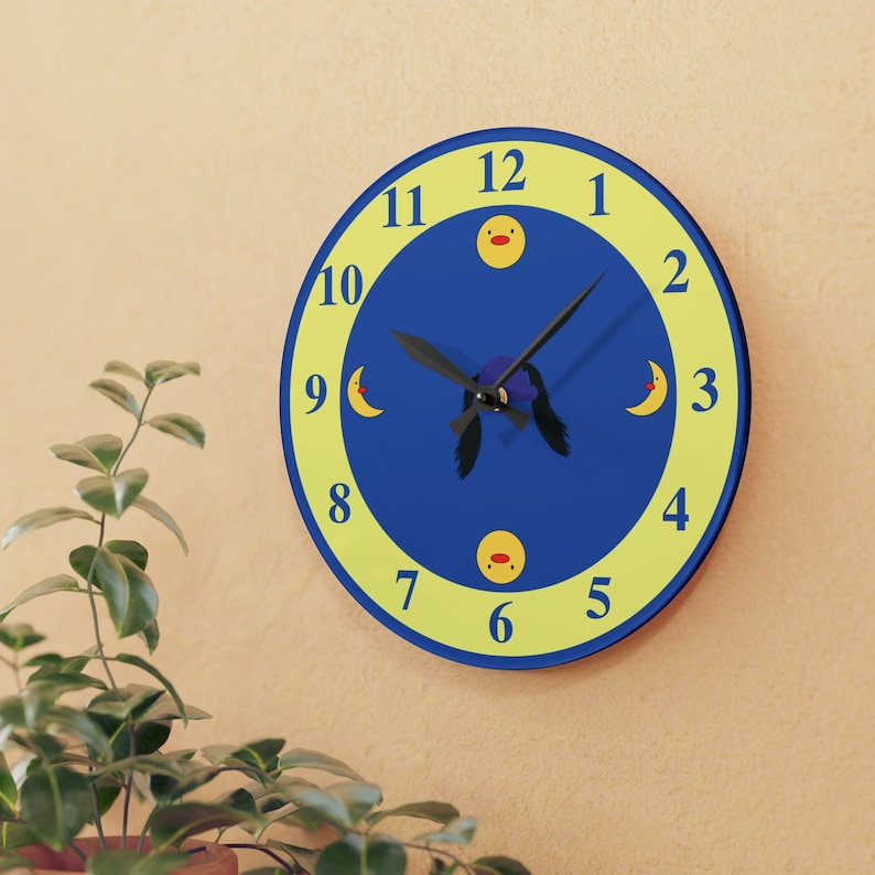 Puede incluir: Un reloj redondo azul y amarillo con una aguja negra y un dise&ntilde;o de pato de dibujos animados. Los n&uacute;meros del 1 al 12 se muestran en la esfera del reloj.