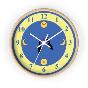 Puede incluir: Un reloj de pared azul y amarillo con una esfera y agujas blancas. El reloj tiene un dise&ntilde;o de pato y luna de dibujos animados. Los n&uacute;meros del 1 al 12 se muestran alrededor de la esfera del reloj.