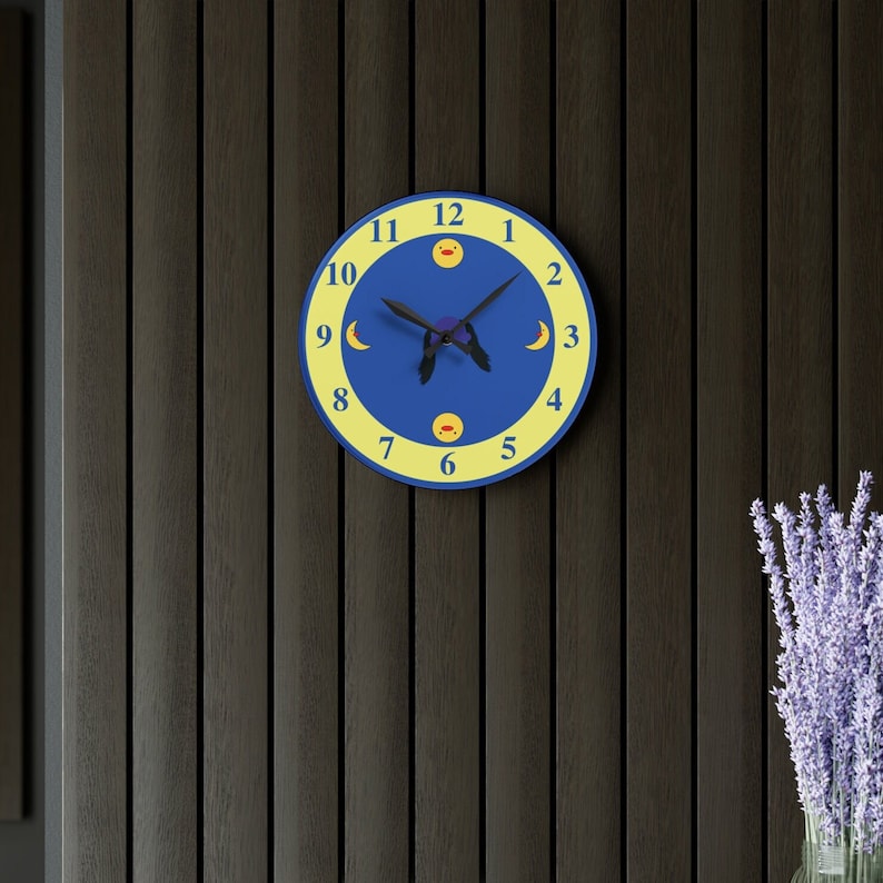 Puede incluir: Un reloj azul y amarillo con un dise&ntilde;o de luna y sol. La esfera del reloj tiene agujas negras y los n&uacute;meros del 1 al 12 est&aacute;n impresos en blanco.