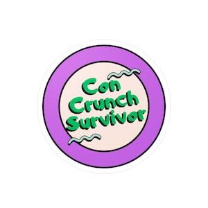 Pode incluir: Um adesivo redondo roxo e branco com o texto "Con Crunch Survivor" em letras verdes.