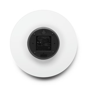 Puede incluir: La parte posterior de un reloj redondo blanco con un mecanismo de reloj negro. El mecanismo del reloj tiene un peque&ntilde;o gancho negro en la parte superior y un peque&ntilde;o bot&oacute;n negro en la parte inferior.