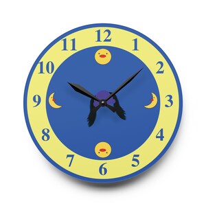 Puede incluir: Un reloj azul y amarillo con manecillas negras y una cara de pato de dibujos animados en el 12. La esfera del reloj tiene un anillo exterior amarillo con n&uacute;meros negros y un c&iacute;rculo interior azul con una luna de dibujos animados y caras de pato.