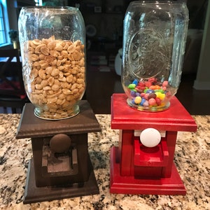 Könnte beinhalten: Zwei selbstgemachte Gummibärchen-Automaten, einer braun und einer rot, mit Glasbehältern gefüllt mit Erdnüssen und bunten Süßigkeiten.