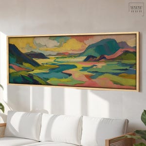 May include: A framed landscape painting with a light wood frame. The artwork features a colourful scene with mountains, a river, and a vibrant sky. The colour palette includes shades of green, blue, yellow, and pink, creating a dynamic and expressive composition.