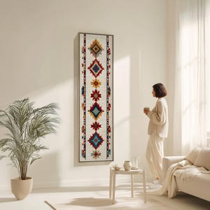 Può includere: Un arazzo da parete rettangolare e lungo con sfondo color crema e un motivo geometrico nei toni del rosso, blu, giallo e marrone. Il design presenta forme a diamante e a stella. L'opera è incorniciata in legno chiaro.