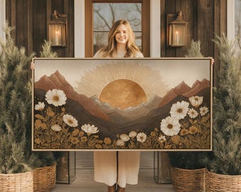 May include: A framed landscape art print featuring a sunrise over mountains and a field of white flowers. The artwork has a warm color palette of browns, tans, and gold. The rectangular print is held up in front of a wooden door.