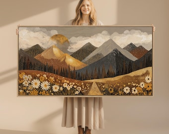 May include: A framed landscape art print featuring a mountain scene with a setting sun, trees, and a field of daisies. The artwork uses a warm color palette of browns, yellows, and blues. The print is held by a person.