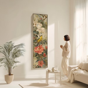 Puede incluir: Una obra de arte enmarcada, larga y vertical, con un diseño floral y de aves. La obra de arte muestra un pájaro amarillo entre flores rojas y blancas y follaje verde. La obra de arte se exhibe en una pared blanca en una habitación bien iluminada.