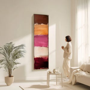 Pode incluir: Obra de arte abstrata com forma retangular, apresentando faixas horizontais de cores: castanho escuro, laranja, magenta, branco sujo e vermelho profundo. A obra está emoldurada e montada numa parede branca, criando uma estética moderna.