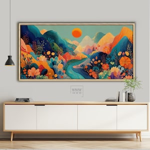 May include: A framed landscape painting with a vibrant, colorful design. The artwork features stylized mountains in shades of blue, orange, and yellow, with a river winding through the scene. An orange sun is in the sky. The painting is displayed above a wooden cabinet.
