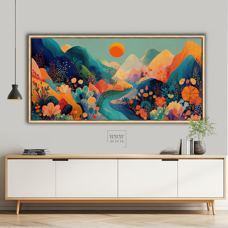 May include: A framed landscape painting with a vibrant, colorful design. The artwork features stylized mountains in shades of blue, orange, and yellow, with a river winding through the scene. An orange sun is in the sky. The painting is displayed above a wooden cabinet.