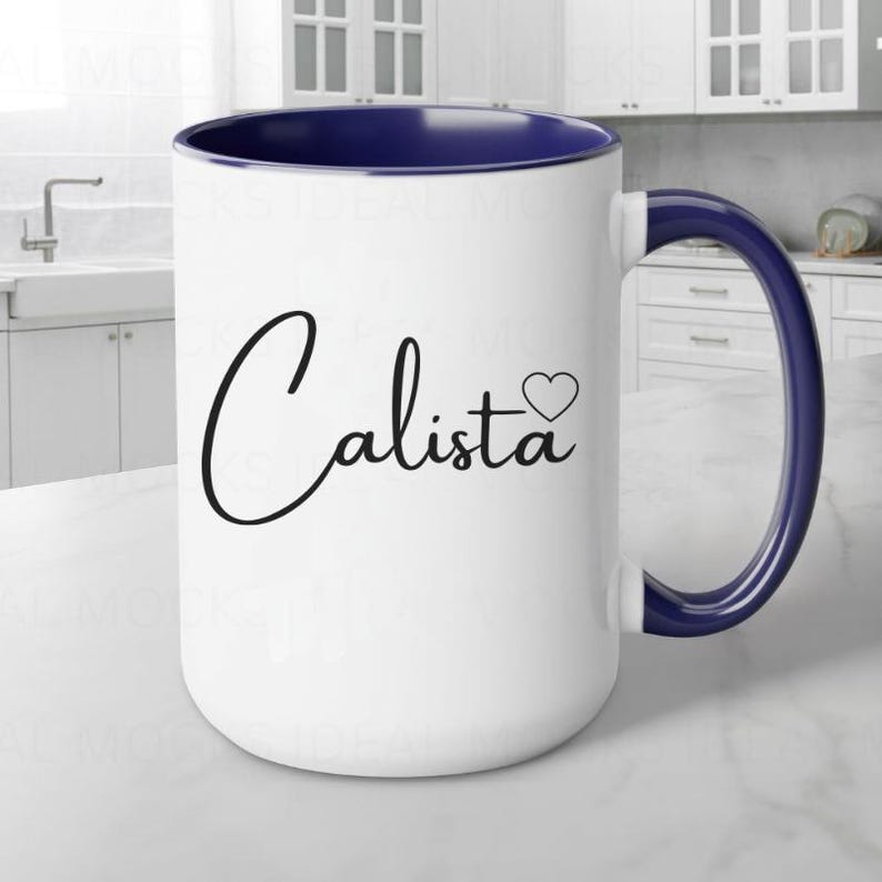 May include: White ceramic mug with a blue rim and handle. The mug has a black cursive design that says "Calista" with a small heart next to it.