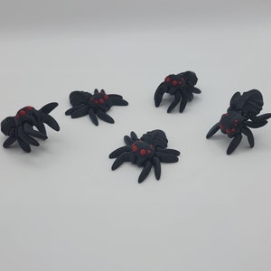 May include: Five black plastic spiders with red eyes. The spiders are posed in different positions on a white background.