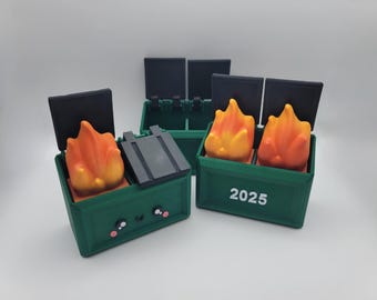 May include: Two green toy dumpsters with black lids. One dumpster has a smiling face and a fire inside. The other dumpster has the year 2025 printed on the front and a fire inside.