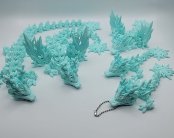Könnte beinhalten: Fünf hellblaue, 3D-gedruckte Drachenfiguren. Die Drachen sind aus einem strukturierten Material gefertigt und haben ein stacheliges, eisiges Aussehen. Ein Drache hat eine silberne Kette daran befestigt.
