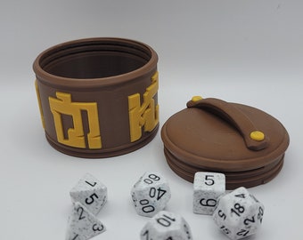 May include: A brown, cylindrical dice box with a lid and a yellow inscription. The box is open and there are seven white dice with black numbers on them.