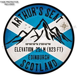 May include: A blue and white circular sticker with the text "Arthur's Seat" in a black circle. The sticker also includes the text "Elevation 251 m (823 ft)", "Edinburgh", and "Scotland". The sticker features a mountain range with a compass rose and a Scottish flag.