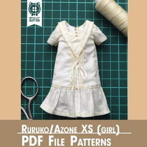 Puede incluir: Vestido blanco con ribete de encaje y un lazo en la parte delantera, sobre una estera de corte verde con un carrete de hilo blanco y unas tijeras. El texto "Ruruko/Azone XS (Girl) PDF File Patterns" está debajo del vestido.