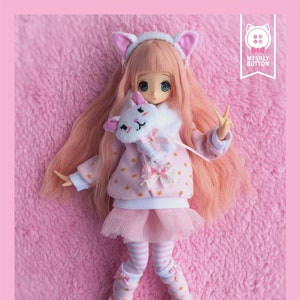 May include: A pink and white doll outfit with a star pattern, a white cat plush toy, and pink and white striped leggings. The outfit is for a doll with a 1/6 scale body. The doll is wearing a pink and white cat ear headband. The outfit is called "Sweet Kitty Set" and is a PDF pattern for the Azon XS body.