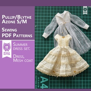 Op de afbeelding: Een naaipatroon voor een zomerjurk en een gaasjas voor een pop. Het patroon is afgedrukt op A4-papier en bevat een snijmat. De jurk is wit met kant en de jas is van wit gaas.