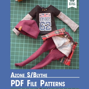Op de afbeelding: Een set poppenkleding voor een Azon S/Blythe pop. De set bevat een zwart-grijs shirt met lange mouwen met een Union Jack en het nummer 62 erop gedrukt, een bordeauxrode muts, een paar bordeauxrode panty's, een blauwe spijkerbroek en een rood-zwart geruit overhemd. De kleding ligt op een groene snijmat.