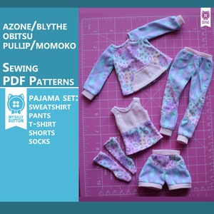 Può includere: Un set di vestiti per bambole per una bambola come Blythe, Obitsu o Pullip. Il set include una felpa, pantaloni, t-shirt, pantaloncini e calzini. Tutti i vestiti sono stampati con un motivo a nuvole blu pastello, rosa e bianco. I vestiti sono disposti su un tappetino da taglio rosa con un righello.