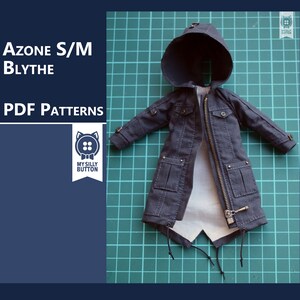 Puede incluir: Una chaqueta gris oscuro con capucha, cierre de cremallera y varios bolsillos, colocada sobre una estera de corte verde. La chaqueta está diseñada para muñecas y está etiquetada como "Azon S/M Blythe PDF Patterns" y "My Silly Button".