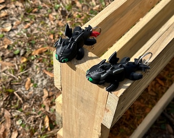 May include: Two black dragon figurines with green eyes and red wings. The dragons are hanging from a wooden surface.