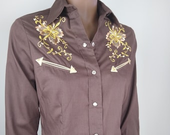 May include: A brown long-sleeved button-down shirt with floral embroidery on the chest and yoke. The shirt has a pointed collar and a single chest pocket.
