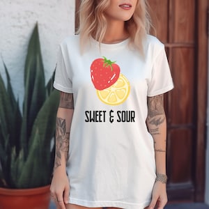 May include: White t-shirt with a graphic of a strawberry and a lemon slice. The text "SWEET & SOUR" is printed below the fruit.