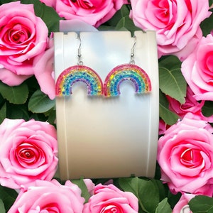 May include: Rainbow-colored beaded earrings shaped like a rainbow arch. The earrings are silver and dangle from the earlobe.
