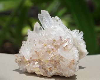 May include: A cluster of clear quartz crystals with a rough, natural texture. The crystals are arranged in a pointed, jagged formation, creating a unique and interesting shape.