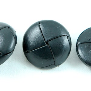 Può includere: Tre bottoni in pelle nera con un design intrecciato. I bottoni sono rotondi e hanno un centro rialzato.